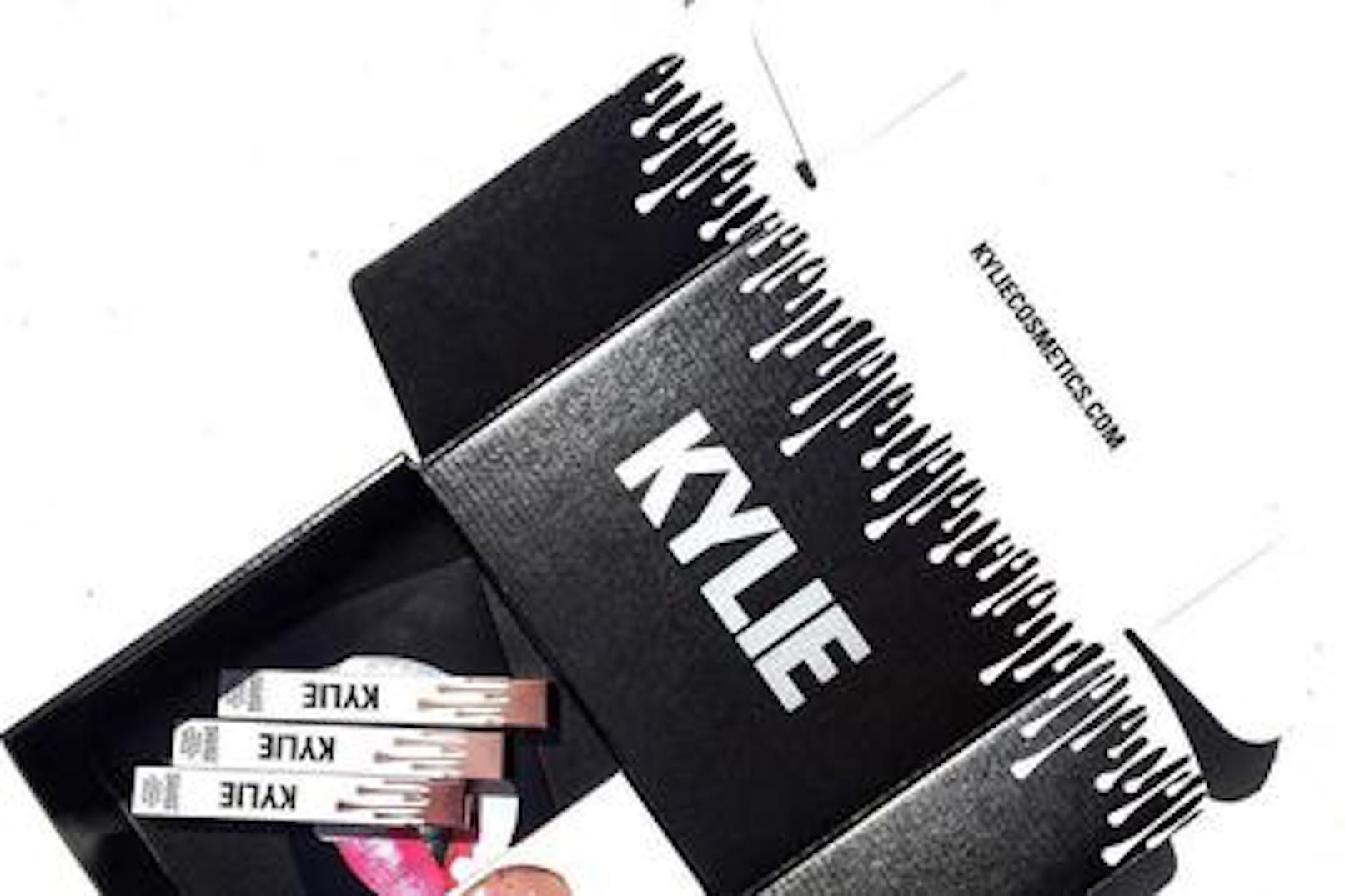 A picture of the Kylie Cosmetics product packaging. This picture is a black box with the kylie lipstick displayed on the front in white. It also has the word 'KYLIE'written in white, and white water looking drops coming down from the top of the box.